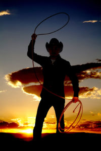 A cowboy is standing in the sunset twirling a rope