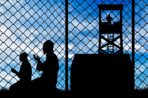 Concept of security. Silhouette of praying refugees and barbed wire fence on the background of the observation tower and stalls