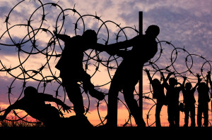 Concept of security. Silhouette of refugees climb over the barbed wire at the border