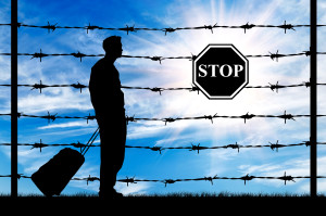 Concept of refugee. Silhouette of a refugee with a bag on a background of a fence with barbed wire and stop sign