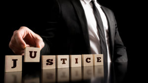 Simple Justice Concept - Close up Businessman in Black Business Suit Arranging Small Wooden Pieces with Justice Text on Black Background.
